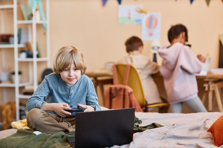Portrait of blonde preteen boy playing videogame on bed with laptop, copy spaceの写真素材