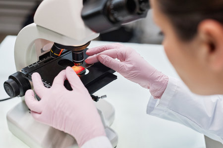 Close up of female scientist putting test material in microscope while doing research in laboratoryの写真素材