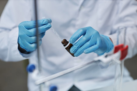 Closeup of scientist holding dropper while doing experiments with medicine in laboratory, copy space
