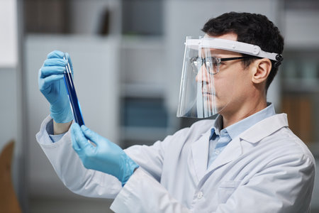 Side view portrait of male scientist wearing face shield in laboratory while doing experiments with...