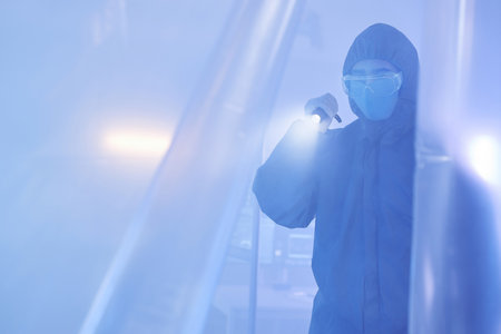 Blue tone portrait of scientist or medical worker wearing full protective suit entering biohazard danger zone with flashlightの写真素材