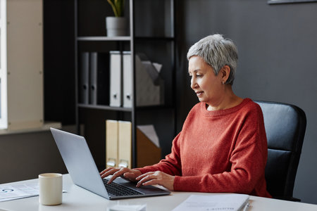 Side view portrait of successful senior businesswoman using computer at workplace in office, copy spaceの写真素材