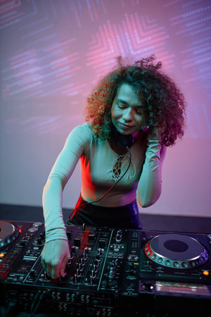 Vertical portrait of young woman as DJ making music tracks at disco party in neon lightの写真素材