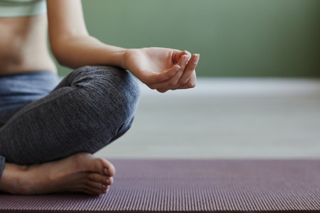 Minimal closeup of young woman meditating sitting in lotus position against green, copy spaceの写真素材