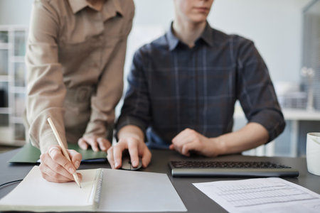 Closeup of young woman taking notes in notebook while reviewing project in office, copy spaceの写真素材
