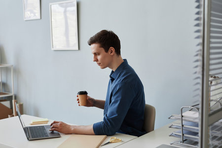 Side view portrait of young man using laptop at workplace in office, copy space
