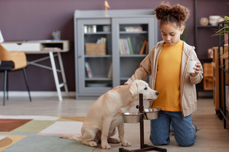 Full length portrait of cute black girl feeding puppy at home and caring for pet, copy space