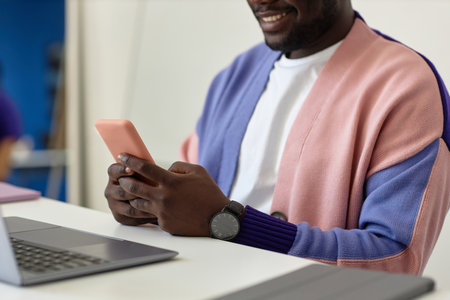 Closeup of smiling black man holding smartphone at workplace in colorful office, copy spaceの写真素材