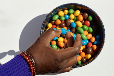 Minimal top view of unrecognizable black man holding colorful candy on white, copy space