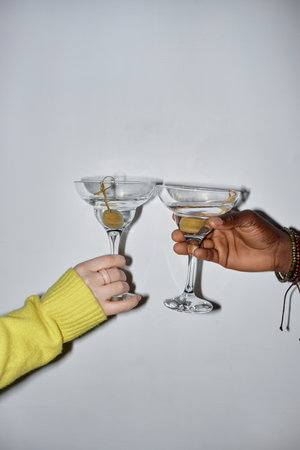 Minimal closeup of two young people holding glasses and toasting drinking martini during party, shot...