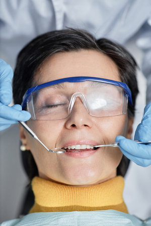 Closeup of mature woman lying in dental chair with eyes closed during teeth examinationの写真素材