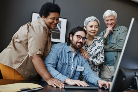 Diverse group of smiling senior people watching man using computer in computer class for elderlyの写真素材