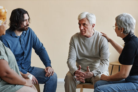Group of senior people sitting in circle at mental health support group with white haired man sharing troublesの写真素材