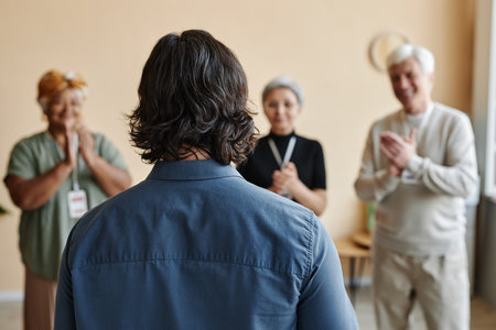 Back view at man presenting in anonymous support group with people applauding