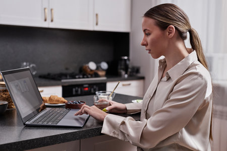 Side view portrait of young woman using laptop and working during breakfast at home, copy spaceの写真素材
