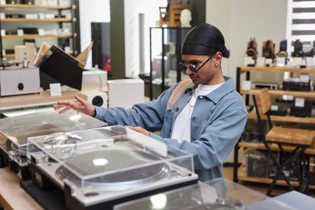 Side view portrait of black young man choosing record player in music store, copy spaceの写真素材