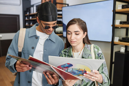 Waist up portrait of smiling young couple holding vinyl records in music storeの写真素材