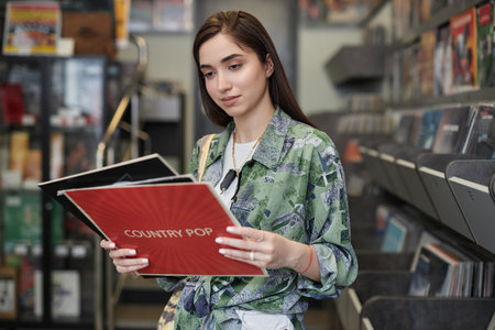 Waist up portrait of young woman choosing vinyl records in record store, copy spaceの写真素材