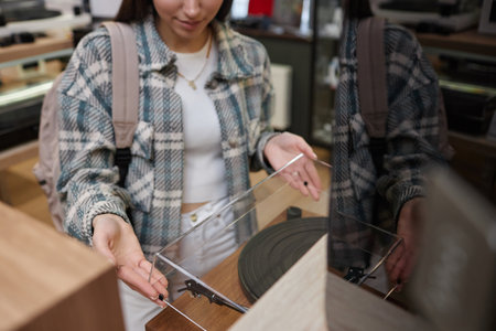 Closeup of young woman opening lid on record player in music store, copy spaceの写真素材