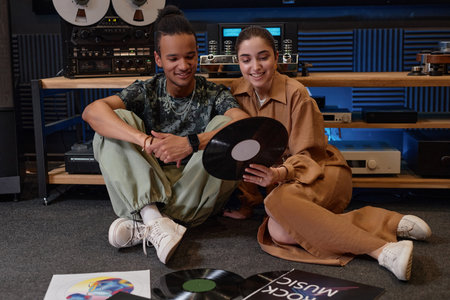 Portrait of smiling young couple choosing vinyl records from home collection sitting on floor...