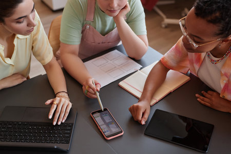 Close up of three young women discussing UI UX design project at meeting table in office and pointing at smartphone screenの写真素材