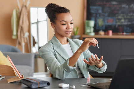 Portrait of elegant black businesswoman doing manicure at workplace in office and using nail polish,...