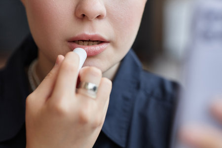 Minimal closeup of young woman doing makeup and using nude lipstick color looking in mirror, copy spaceの写真素材
