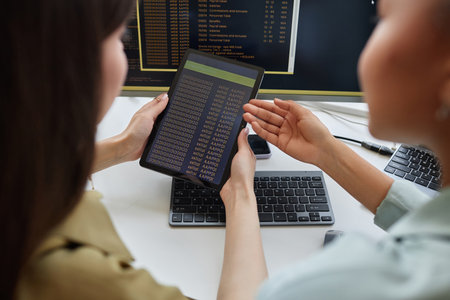 Closeup of two young women holding digital tablet with code, copy space