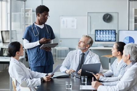 Young confident African American male intern with tablet making speech or report upon medical topic...