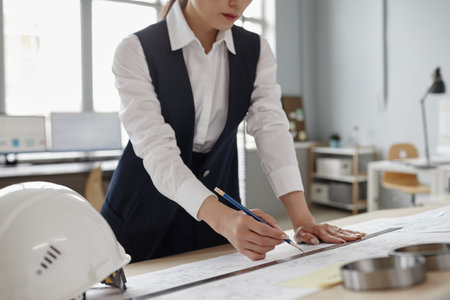 Closeup of female engineer drawing blueprints and plans at workstation in office, copy spaceの写真素材