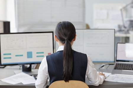 Back view of woman working as female engineer using computer with blueprints on screens, copy spaceの写真素材