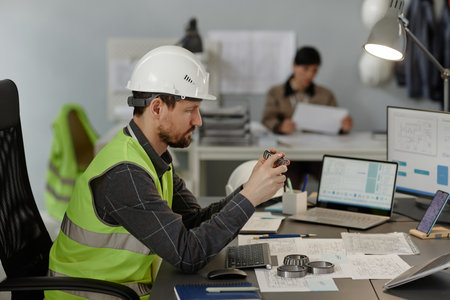Side view portrait of male engineer holding steel bearing machine part while working on construction...