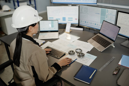 High angle portrait of female engineer wearing hardhat at workplace in office and using multiple computers, copy spaceの写真素材