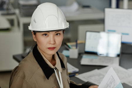 Closeup portrait of Asian woman wearing hardhat at workplace in office and looking at camera, copy...