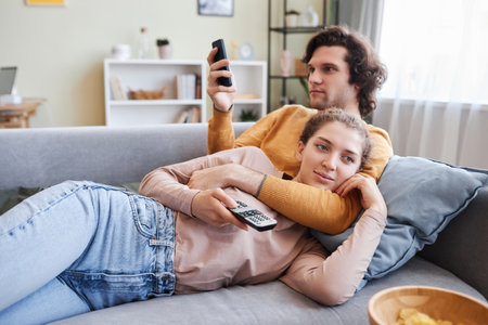 Portrait of young couple cuddling on sofa at home and watching TV together, copy spaceの写真素材