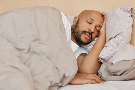 Portrait of adult black man sleeping in comfortable bed in cozy homeの写真素材