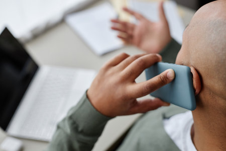 Closeup of adult black man speaking by smartphone while working,focus on foreground, copy space