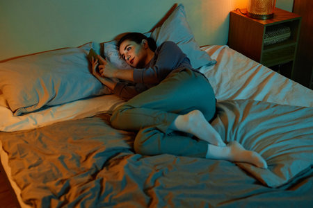 Full length portrait of lonely adult woman using smartphone in bed at night and scrolling social media, copy spaceの写真素材