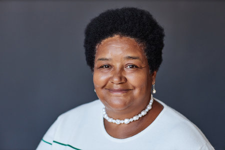 Portrait of aged African American woman in white pullover, pearl necklace and earrings looking at...