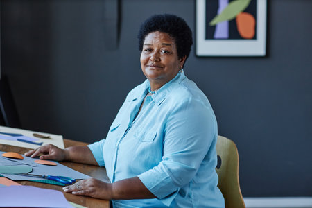 Confident mature African American craftswoman sitting by workplace in studio and looking at camera...
