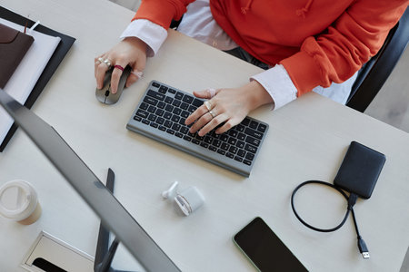 Above view of hands of young female white collar worker pressing keys of computer keyboard and...