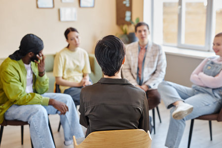 Rear view of specialist sitting on chair and talking to young people during psychotherapy in officeの写真素材