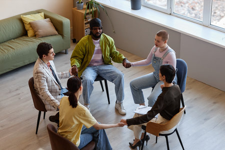 High angle view of group of people holding hands while sitting at psychotherapy sessionの写真素材