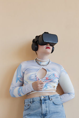 Vertical image of young woman in wireless VR glasses standing against beige backgroundの写真素材