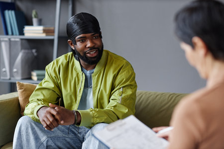 African American man discussing problems with specialist while sitting on sofa in officeの写真素材
