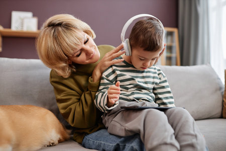 Loving mother putting headphones on little boy with down syndrome using laptop at homeの写真素材