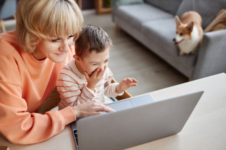 Top view portrait of happy little boy with down syndrome using computer while studying at home with momの写真素材