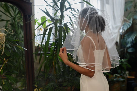 Portrait of black young woman as young bride wearing wedding gown and looking in mirrorの写真素材
