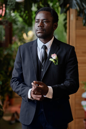 Vertical portrait of handsome black man getting ready for wedding ceremony and adjusting tuxの写真素材