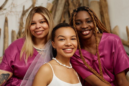 Waist up portrait of happy black woman as young bride having fun with bridesmaids during wedding and looking at cameraの写真素材